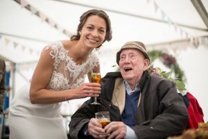 A joyful wedding moment shared between guests during a reception under a tent with drinks.