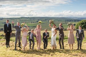 Wedding party poses jubilantly on a hilltop with scenic countryside views in the background.