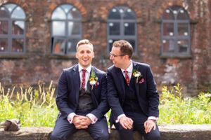 Two grooms in matching dark suits share a happy moment on their wedding day.
