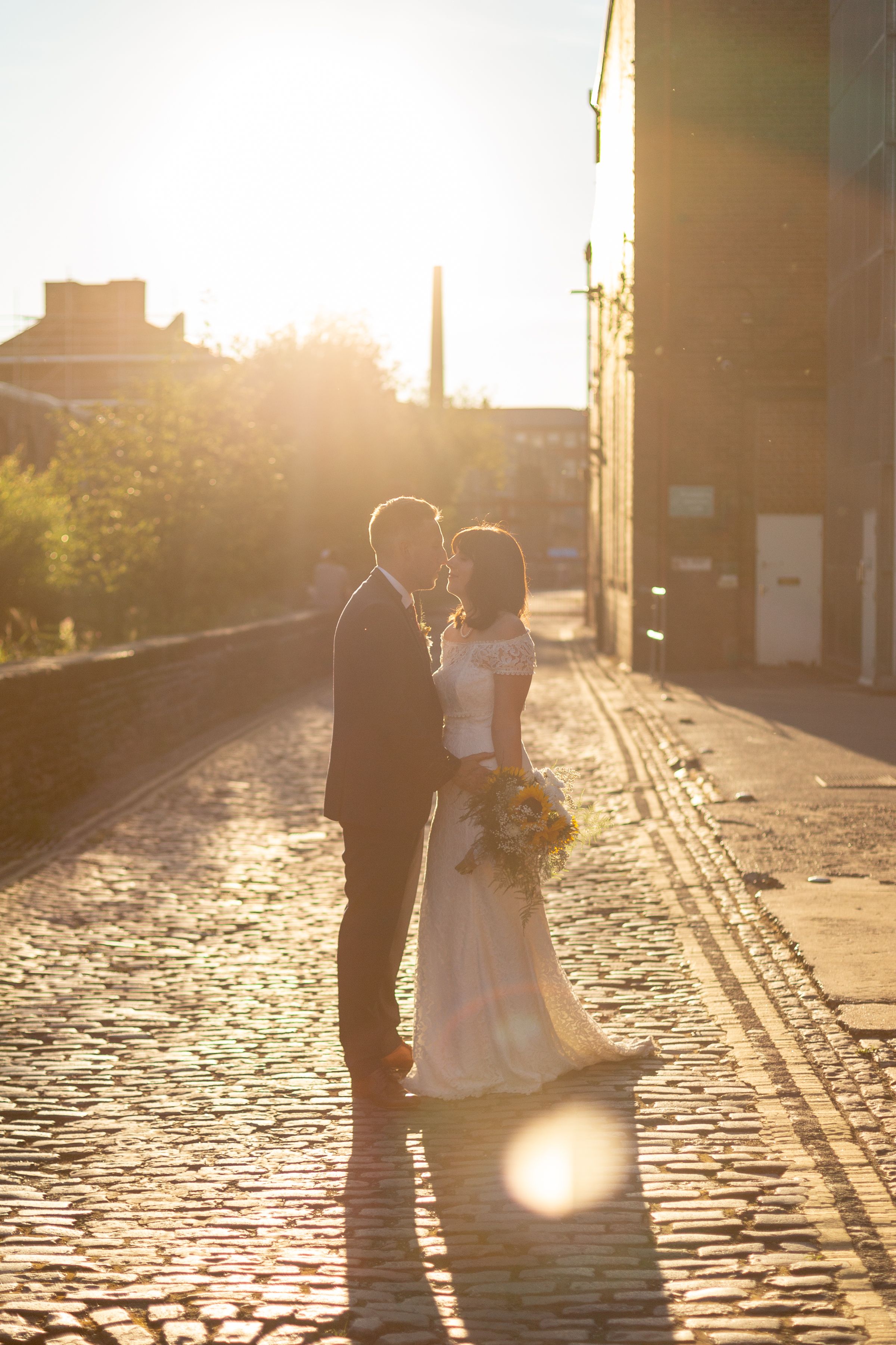 Silhouetted couple shares intimate moment on cobblestone street during golden hour.