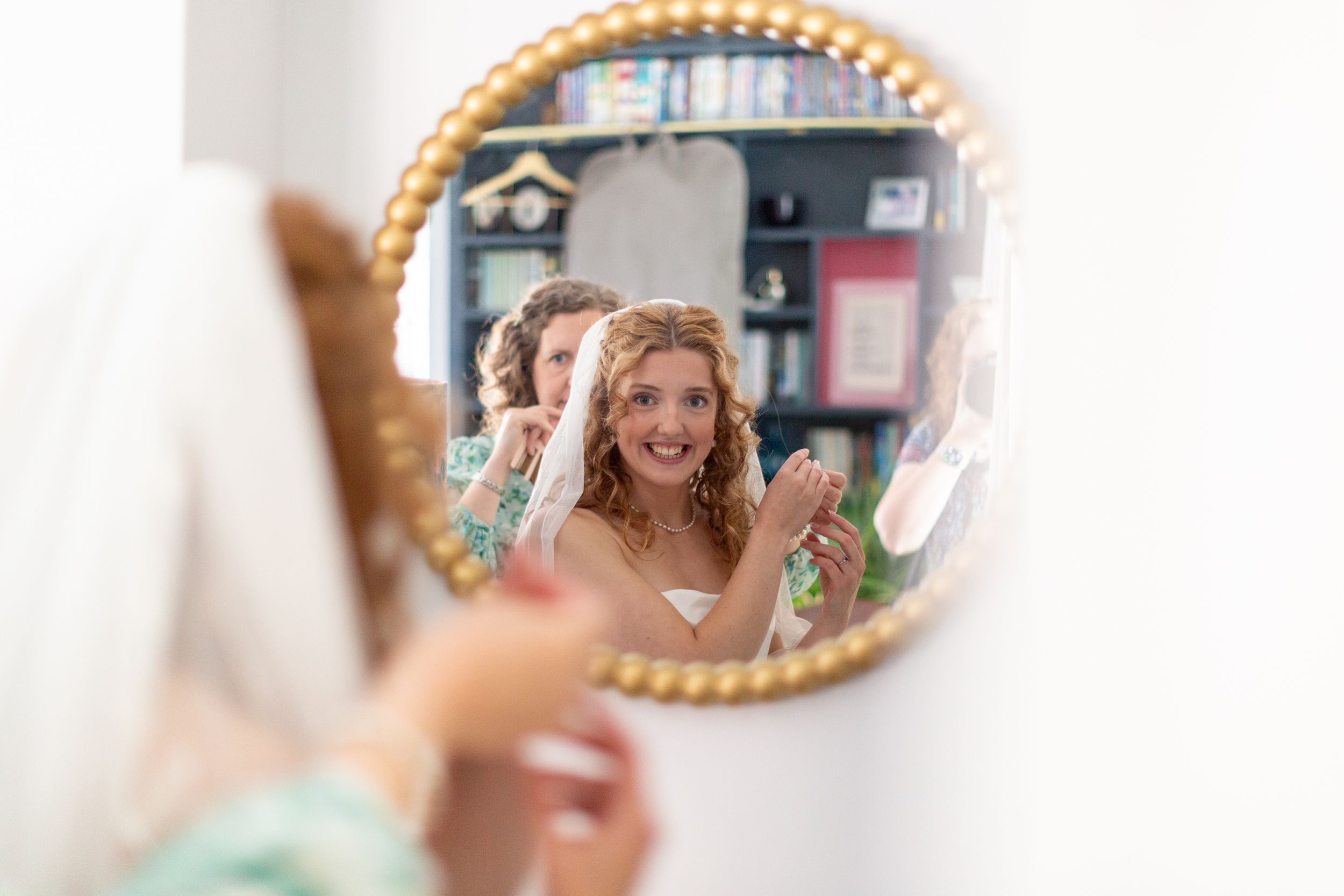 A person holding a phone takes a selfie photo in front of a decorative round mirror mounted on a wall.