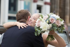 Wedding bouquet with pink and white roses while couple embraces.