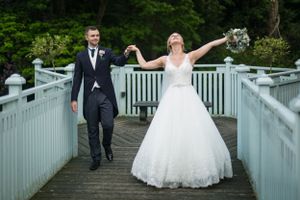Celebratory pose by newlyweds on white wooden bridge surrounded by greenery.