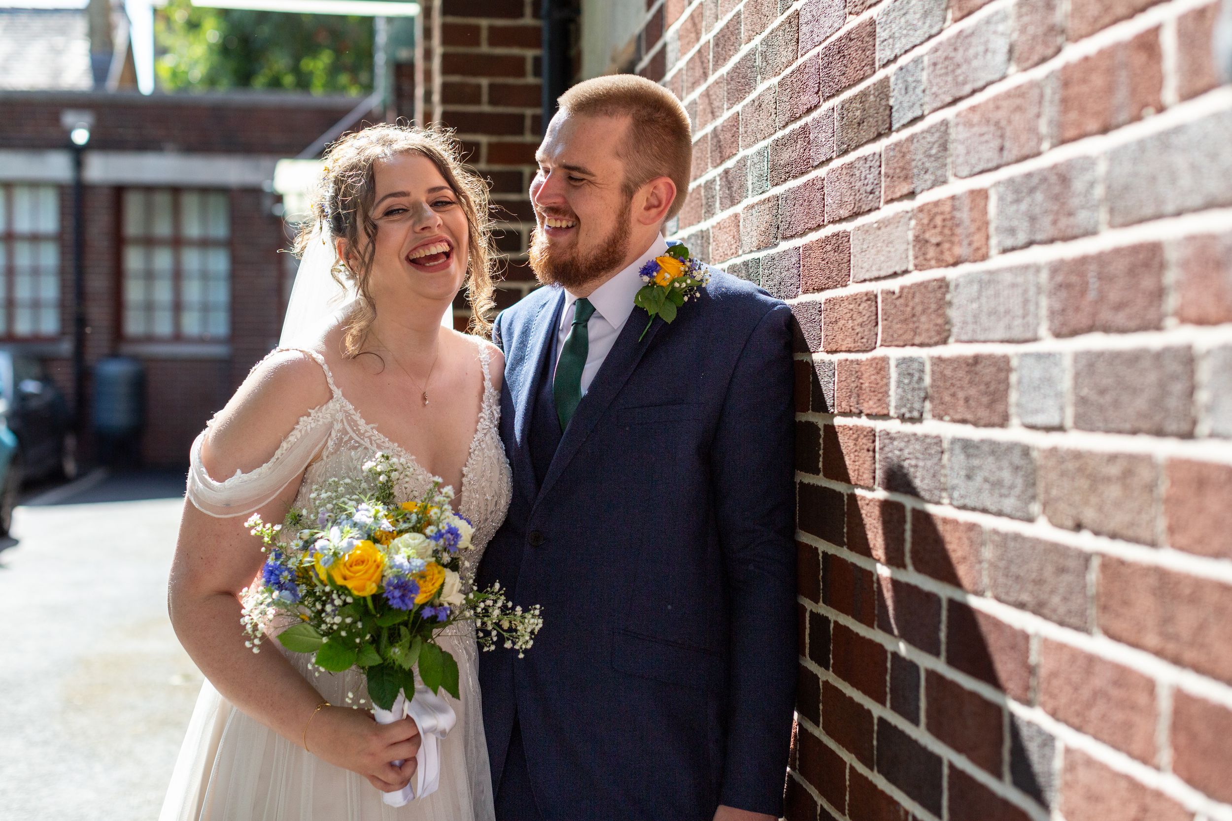 A joyful wedding moment captured against a brick wall with a colorful bouquet.
