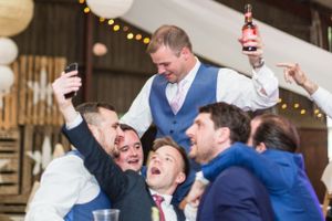 Groomsmen celebrating with drinks and laughter during wedding reception.