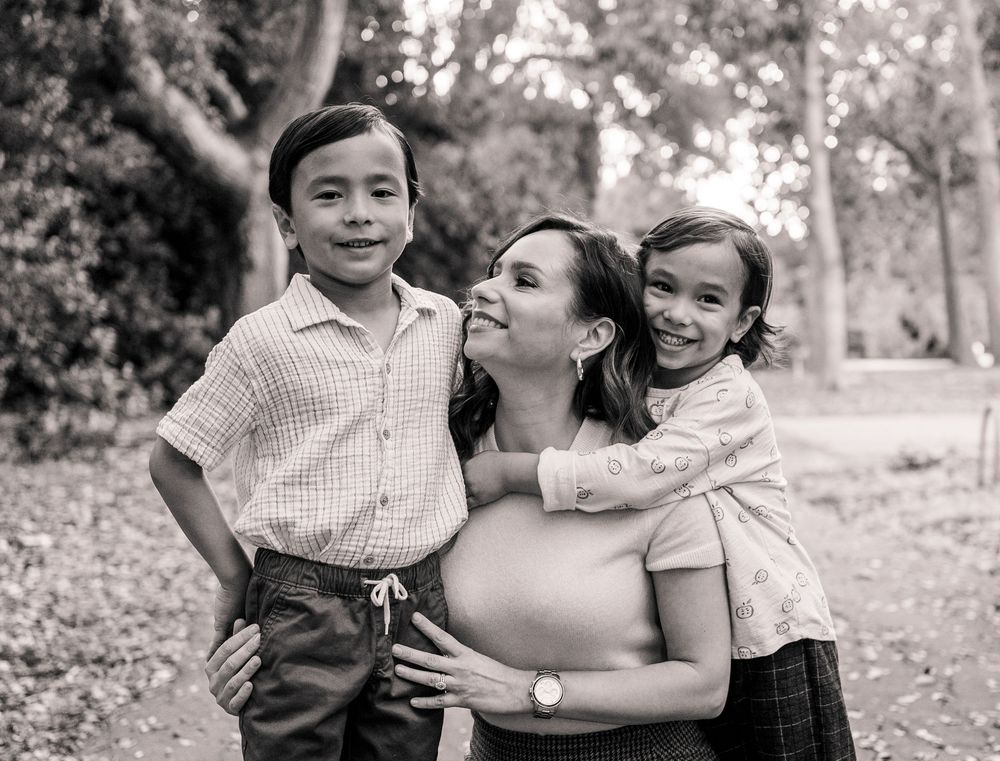 Black and white portrait of smiling mother with two young children in park.