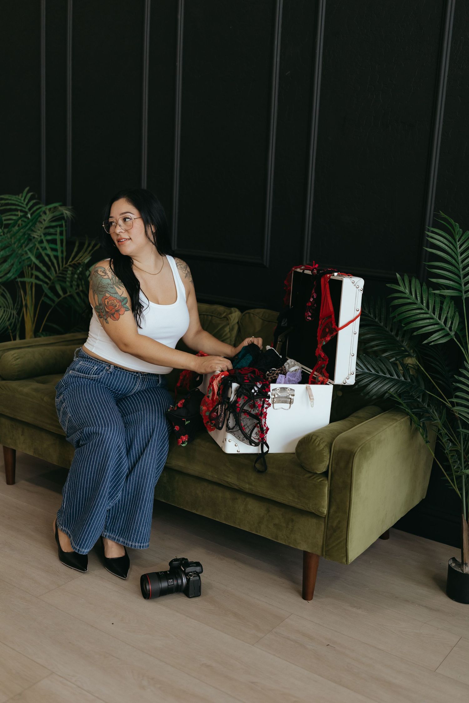 woman sitting on a green couch indoors, a white trunk open is on the couch next to her.