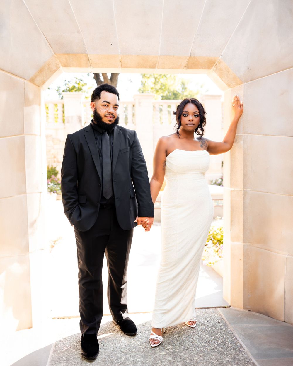 A couple in wedding attire poses playfully in a bright white corridor during their wedding photoshoot.