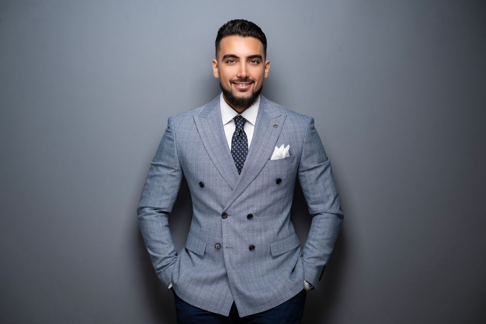 Business professional wearing gray double-breasted suit posed against dark background.