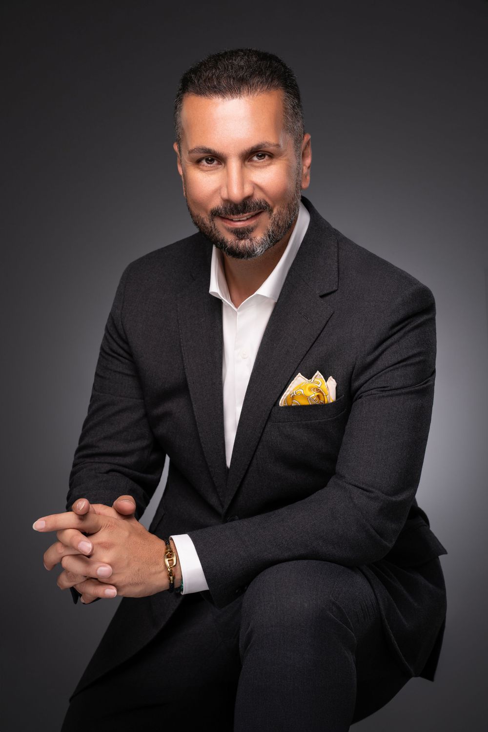 Executive in black suit with yellow pocket square posed in studio portrait.