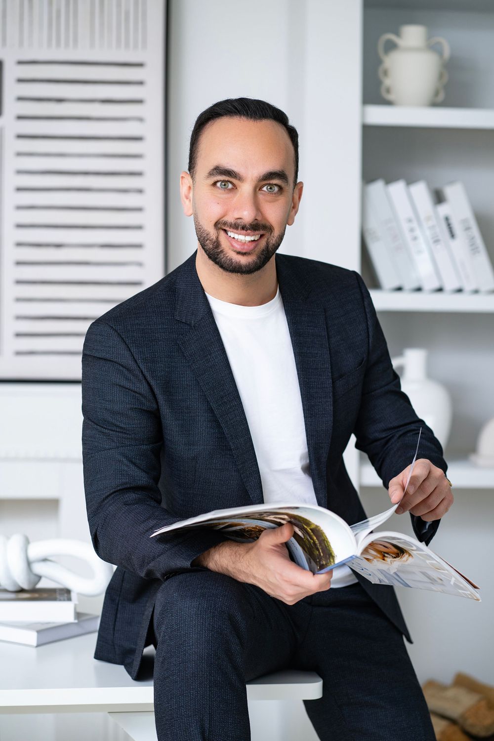 Professional man in blazer smiling while reading magazine in modern white office setting.