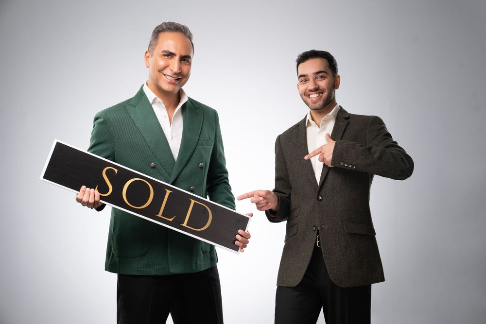 Real estate professionals in suits holding sold sign against gray background.