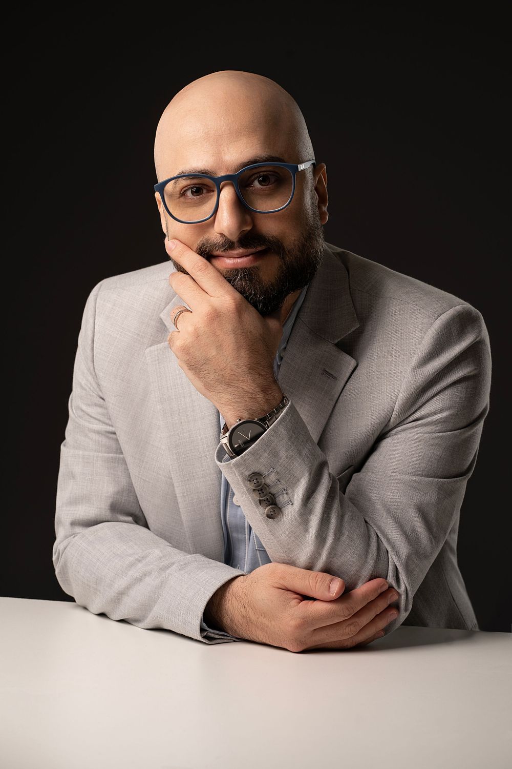 Man in glasses and gray suit jacket posing thoughtfully against dark background in business headshots.