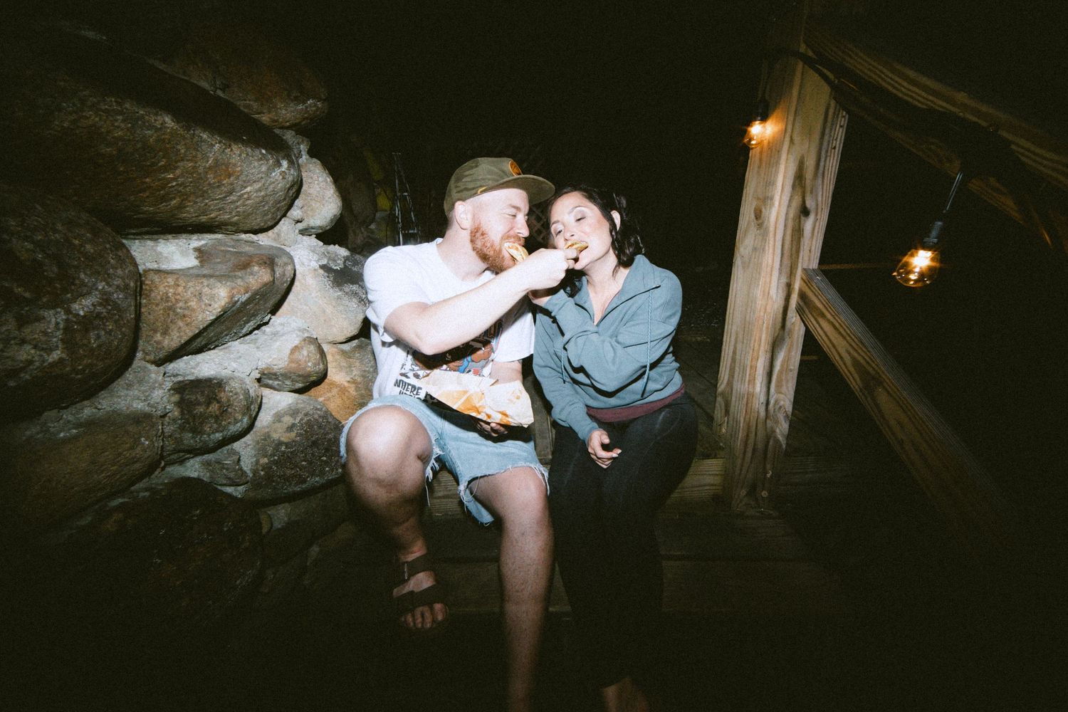 A candid nighttime moment between a couple sitting against a stone wall.