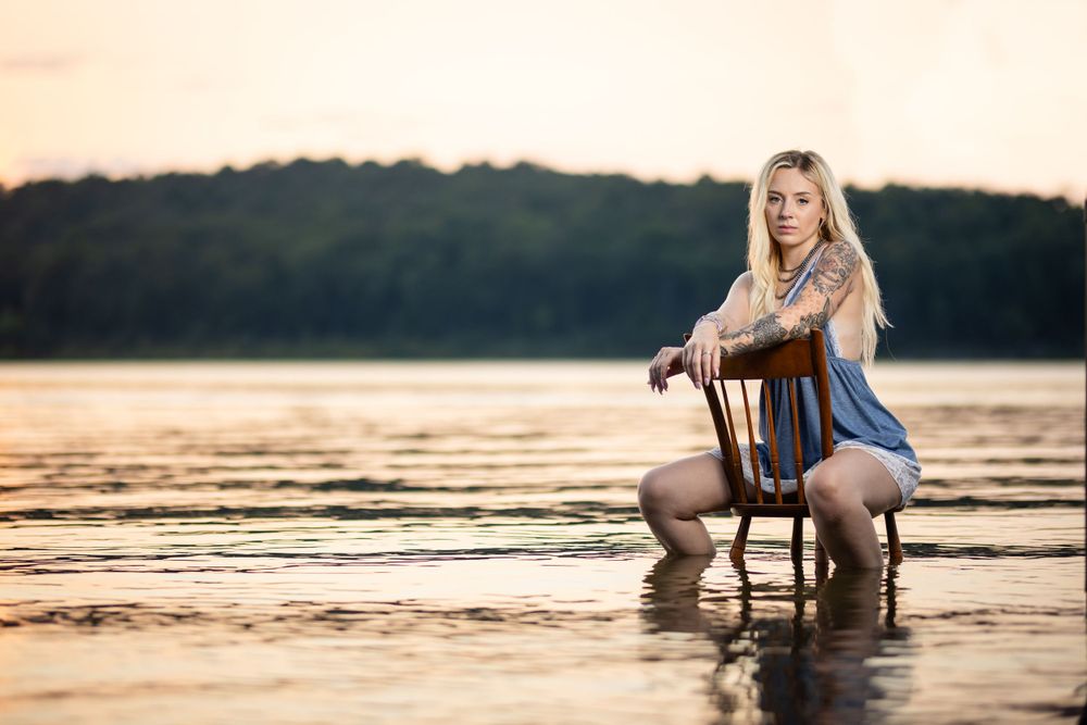 Young woman seated in the shallow water of Norfork Lake at sunset for a portrait session