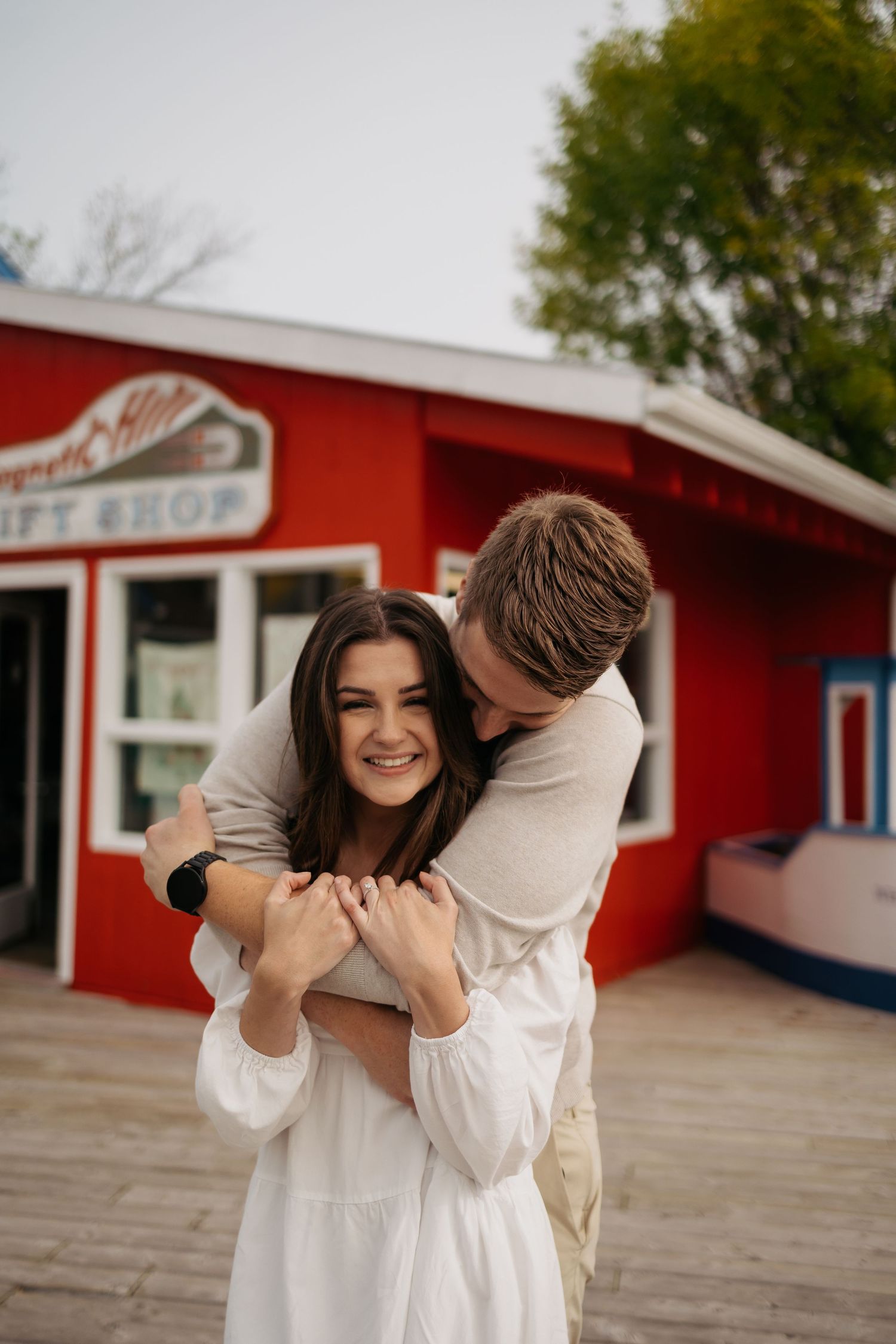 Playful couple embracing outside a red gift shop building.