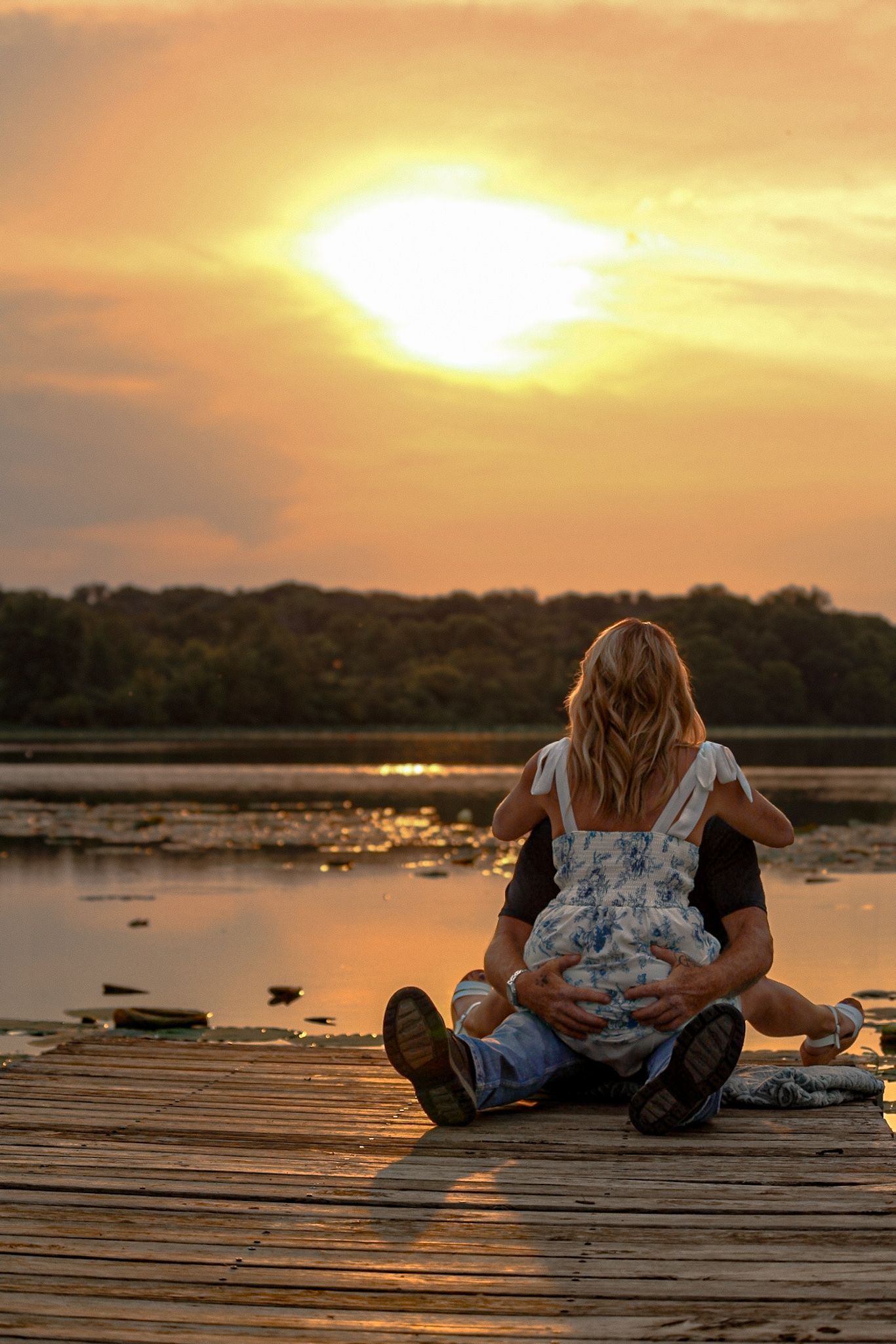 Two figures silhouetted on a wooden dock during a serene lakeside sunset.
