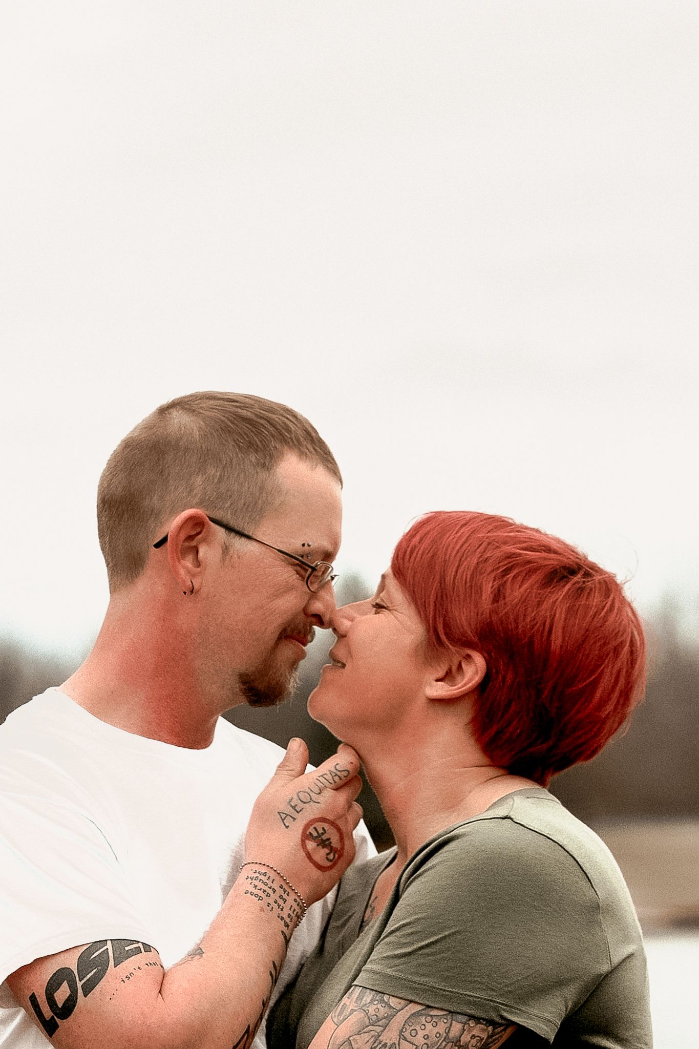 Close-up of a couple with tattoos sharing an intimate moment outdoors.