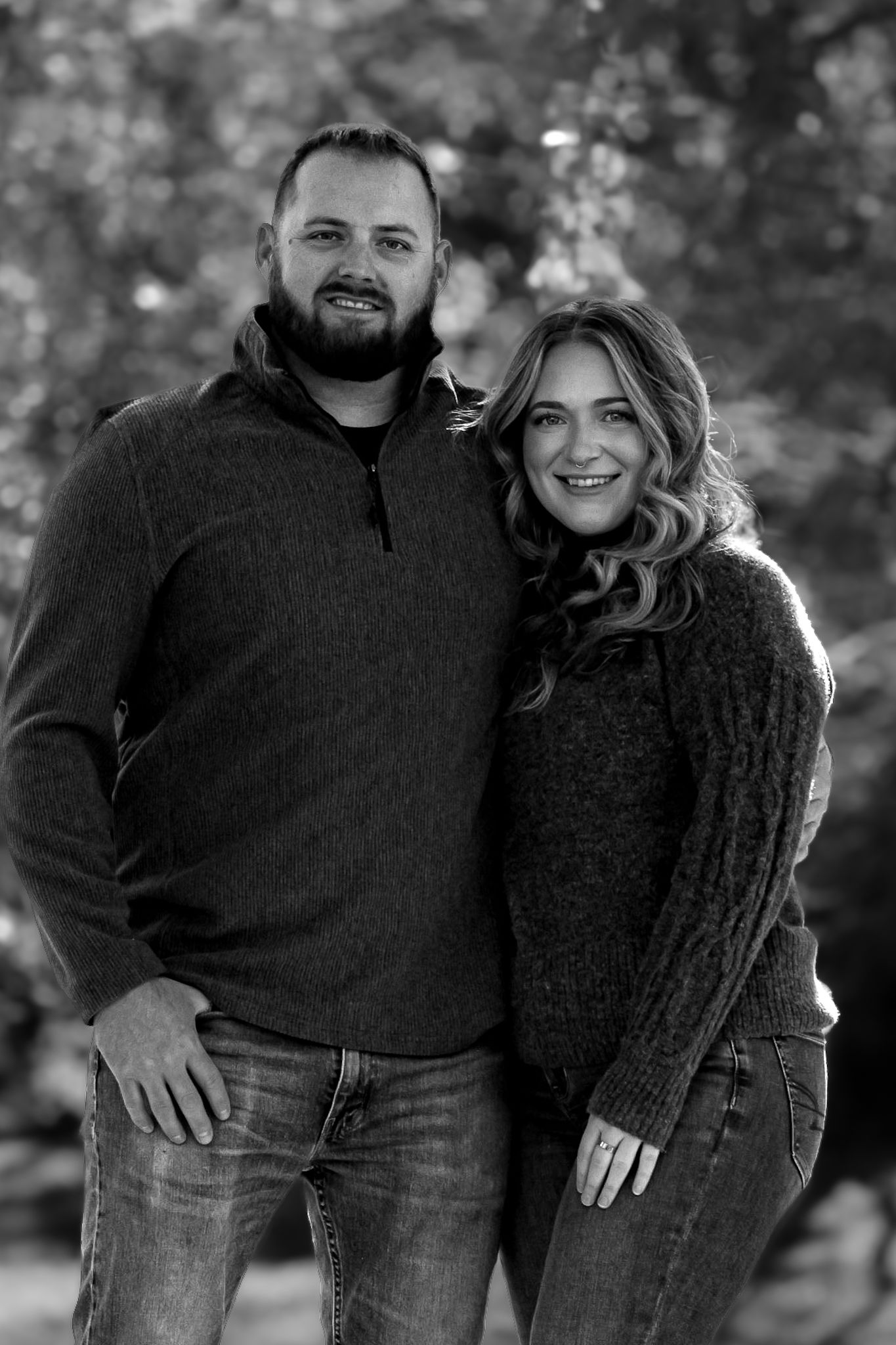 A black and white portrait of a couple in casual sweaters against a blurred outdoor background.