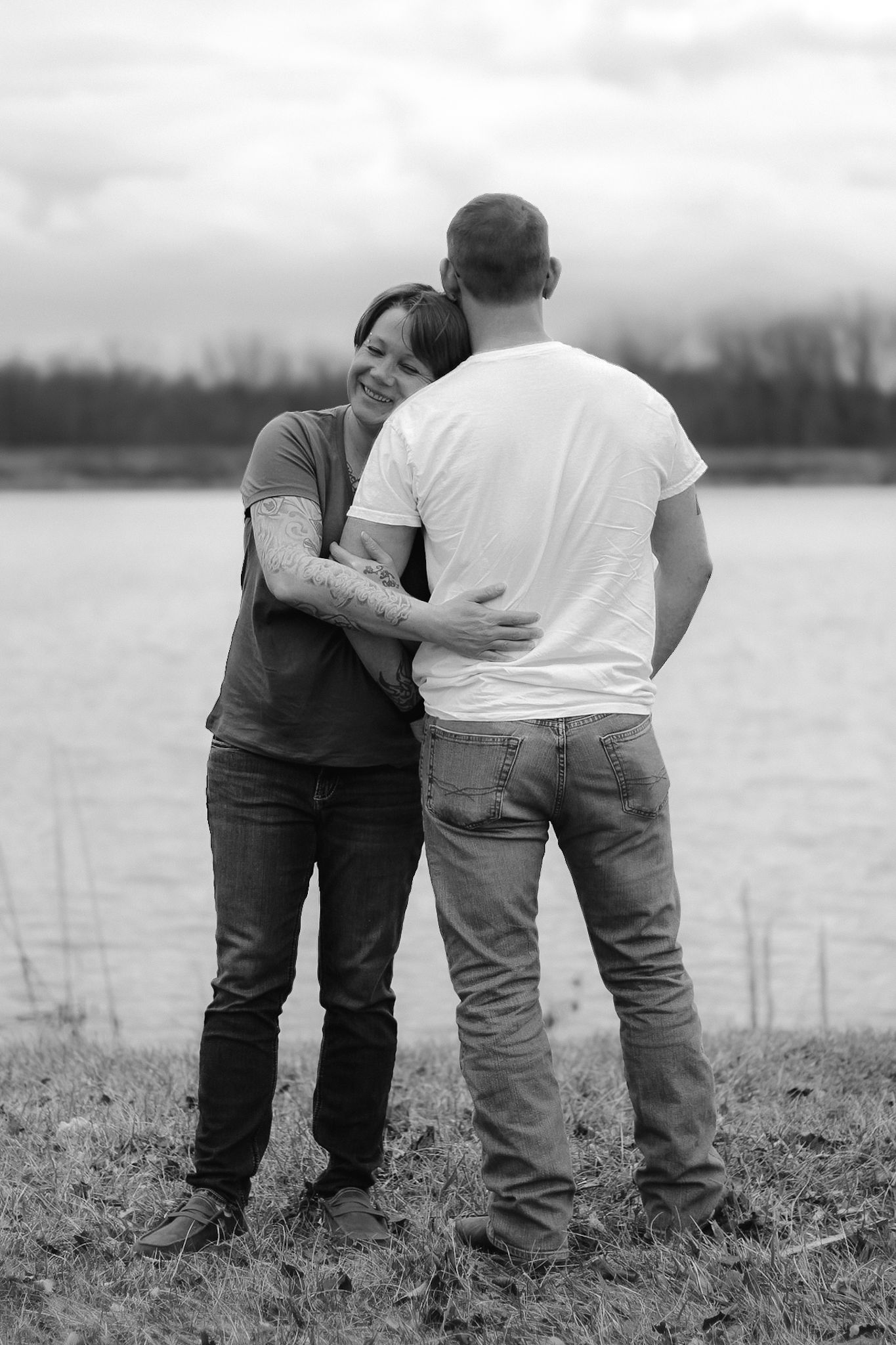 Black and white photo of a couple embracing by a lake.