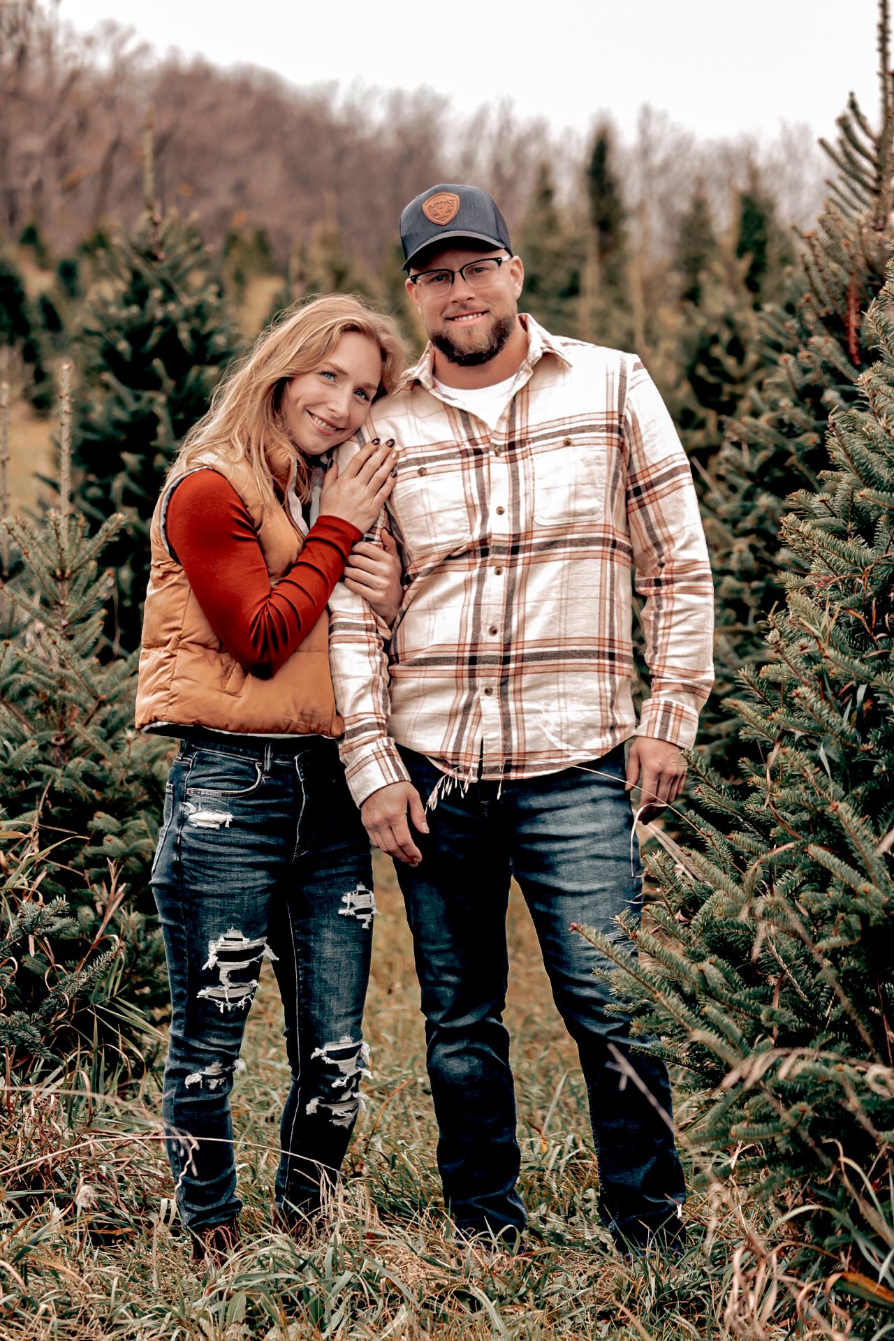 Couple in casual winter wear posing together among Christmas trees.