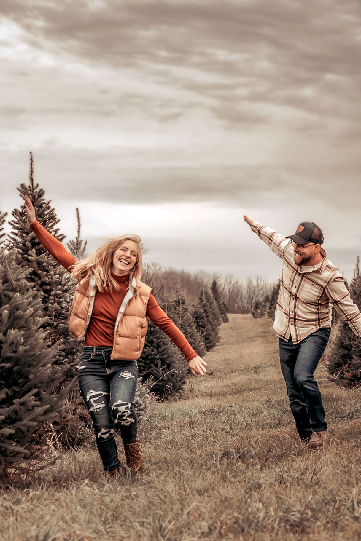 Playful couple with arms outstretched having fun in Christmas tree farm.