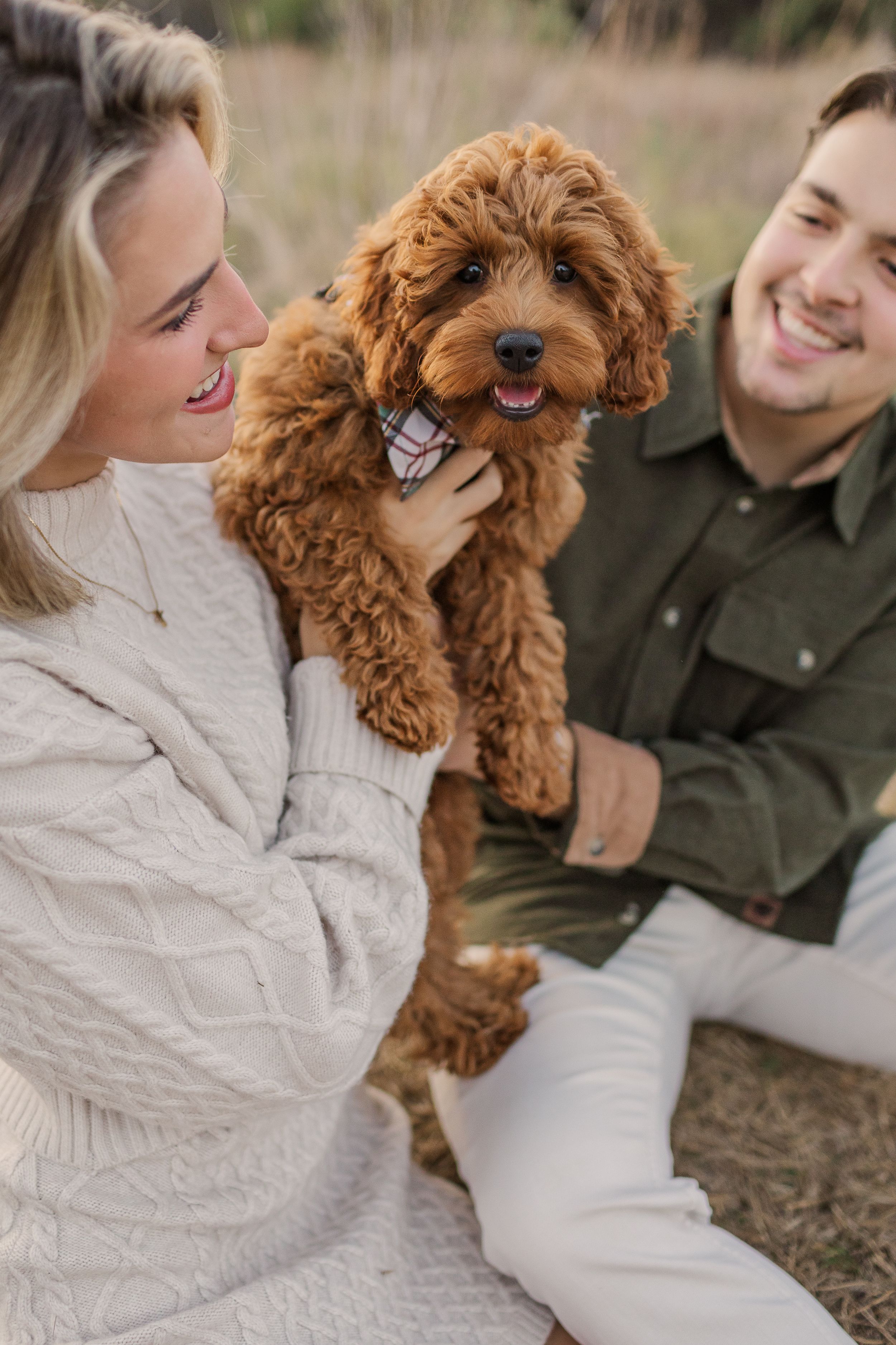 A couple shares joyful moments with their playful red Goldendoodle dog outdoors in a candid photo series, by best San Antonio Photographer.