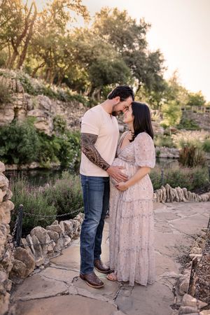 Couple in love embrace during golden hour in a romantic garden setting with rustic stone walls. San Antonio Maternity Photographer