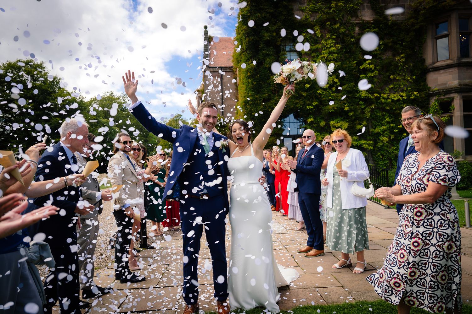 Wedding guests throw confetti as the newlyweds walk through a celebratory outdoor reception line.