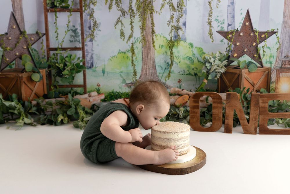 A small child in dark clothing leans over a cake smash setup with rustic star decorations and greenery in the background.