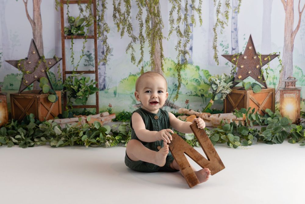 A baby sitting on a white floor with plush toy surrounded by rustic stars and greenery decorations.