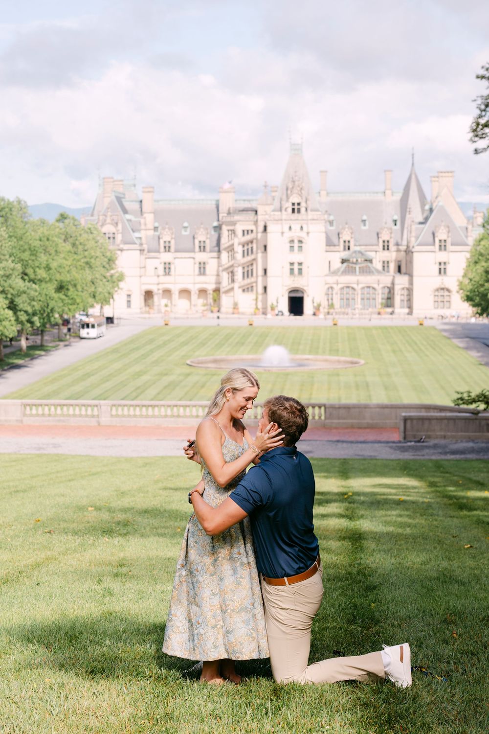 Man kneeling to propose to woman on lawn in front of Biltmore Estate in Asheville, NC.