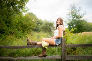 Person sitting casually on a rustic wooden fence in a countryside setting.