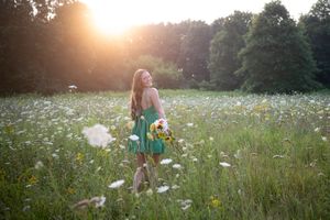 Young woman in green dress holding sunflowers walks through a sunlit wildflower meadow at golden hour.