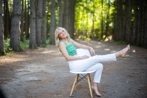 Person in casual attire lounging on modern chair in wooded setting.