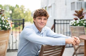 Person in light blue shirt sitting casually on outdoor wooden bench.