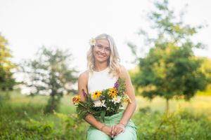 A person in casual attire holds a vibrant bouquet of flowers while sitting outdoors in a sunny natural setting.