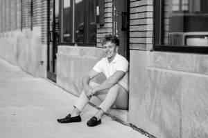 Black and white portrait of person sitting against brick wall in classic outfit.