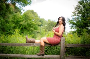 Person in brown dress reclining on wooden bench surrounded by lush greenery.