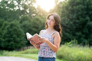 Person reading book outdoors in floral top during golden hour sunset.