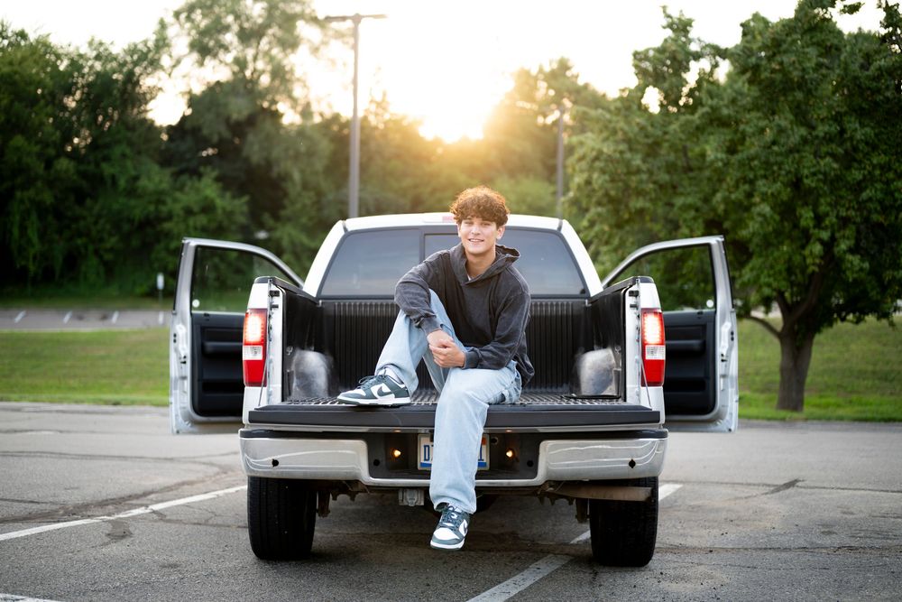 Casual portrait sitting in pickup truck bed during golden hour sunset.