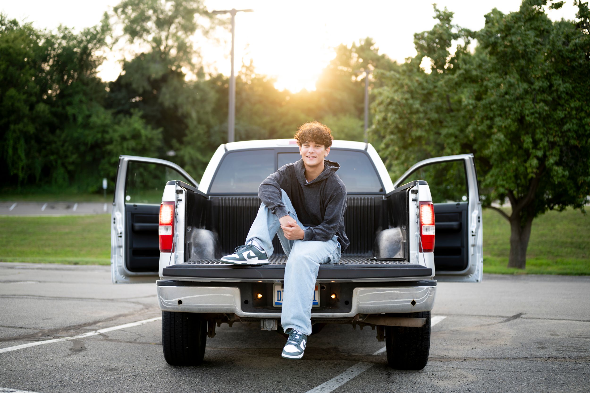 Casual portrait sitting in pickup truck bed during golden hour sunset.