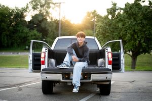 Casual portrait sitting in pickup truck bed during golden hour sunset.