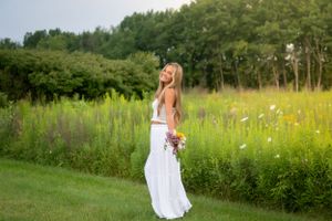A flowing white dress contrasts beautifully against lush green meadow and trees.