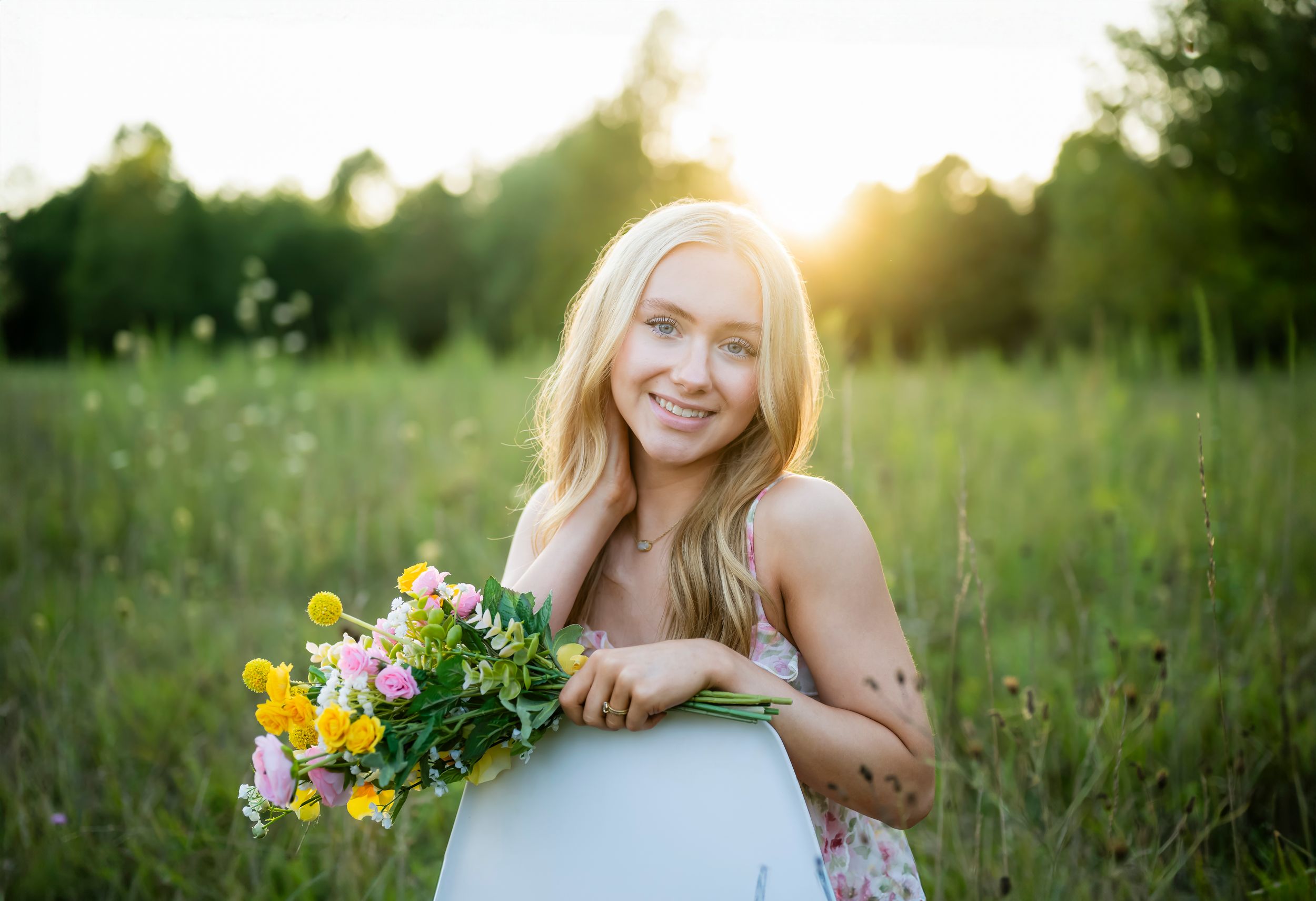 Smiling blonde woman holding colorful spring flowers in a sunlit green meadow at golden hour.