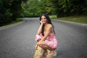 Person in casual attire sitting on asphalt road during outdoor photoshoot.