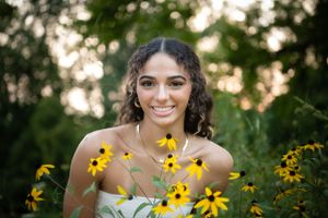 Person posing with bright yellow black-eyed susan flowers in natural outdoor setting.