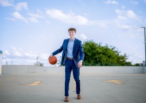 Teen boy in blue suit holding basketball on rooftop under blue sky.