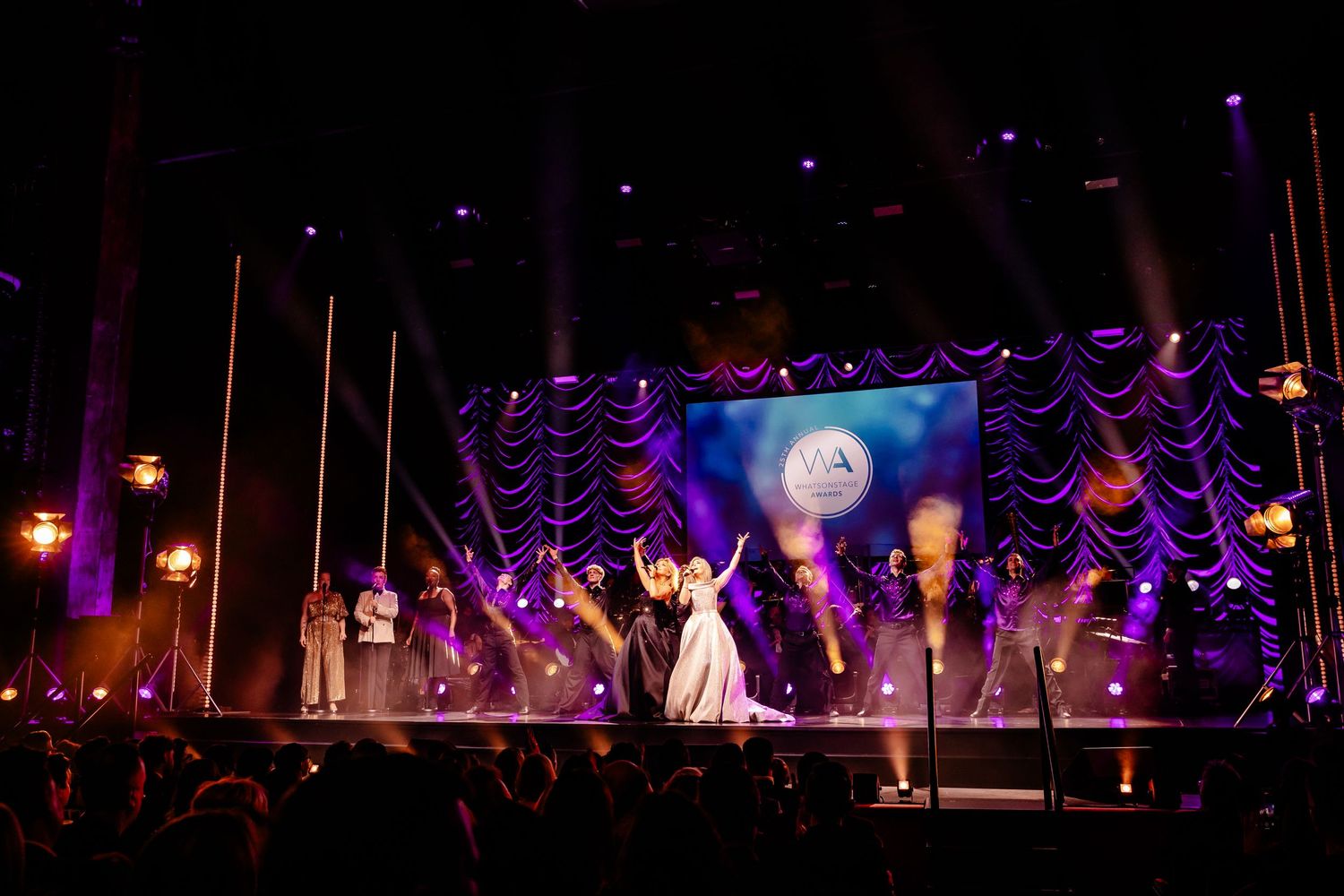Dramatic stage performance with purple lighting effects and silhouetted performers on a darkened theatrical stage.