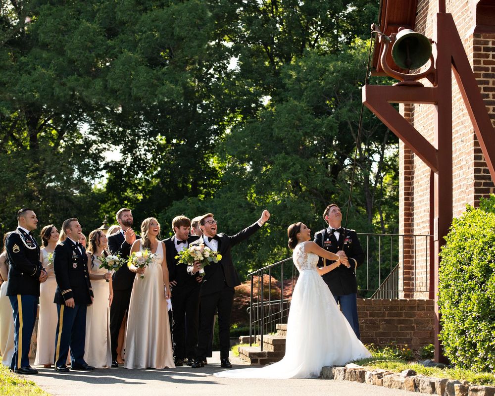 Wedding party gathers outside brick church with bridesmaids in long gowns and groomsmen during outdoor summer ceremony.